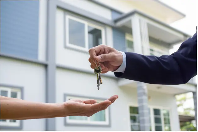 A real estate agent handing over keys to a new homeowner in front of a modern house, symbolizing the completion of a property sale